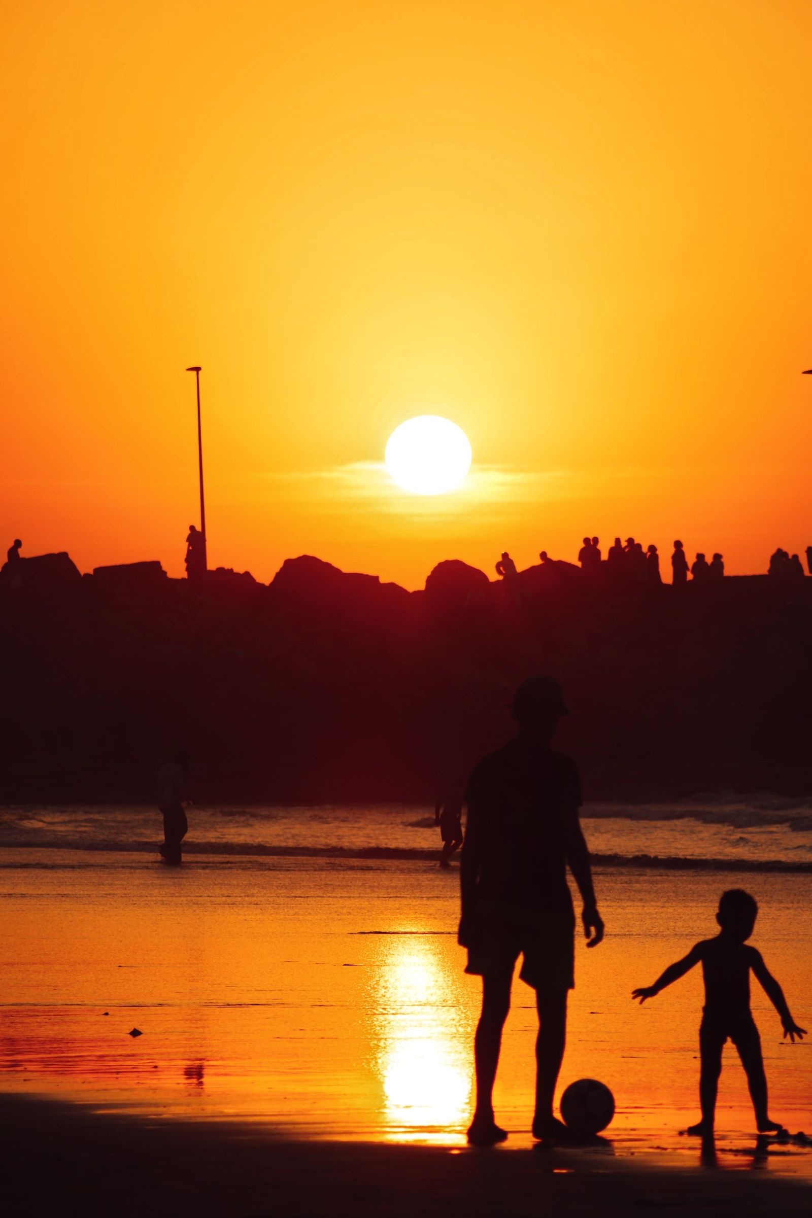 A parent and child playing with a soccer ball at sunset